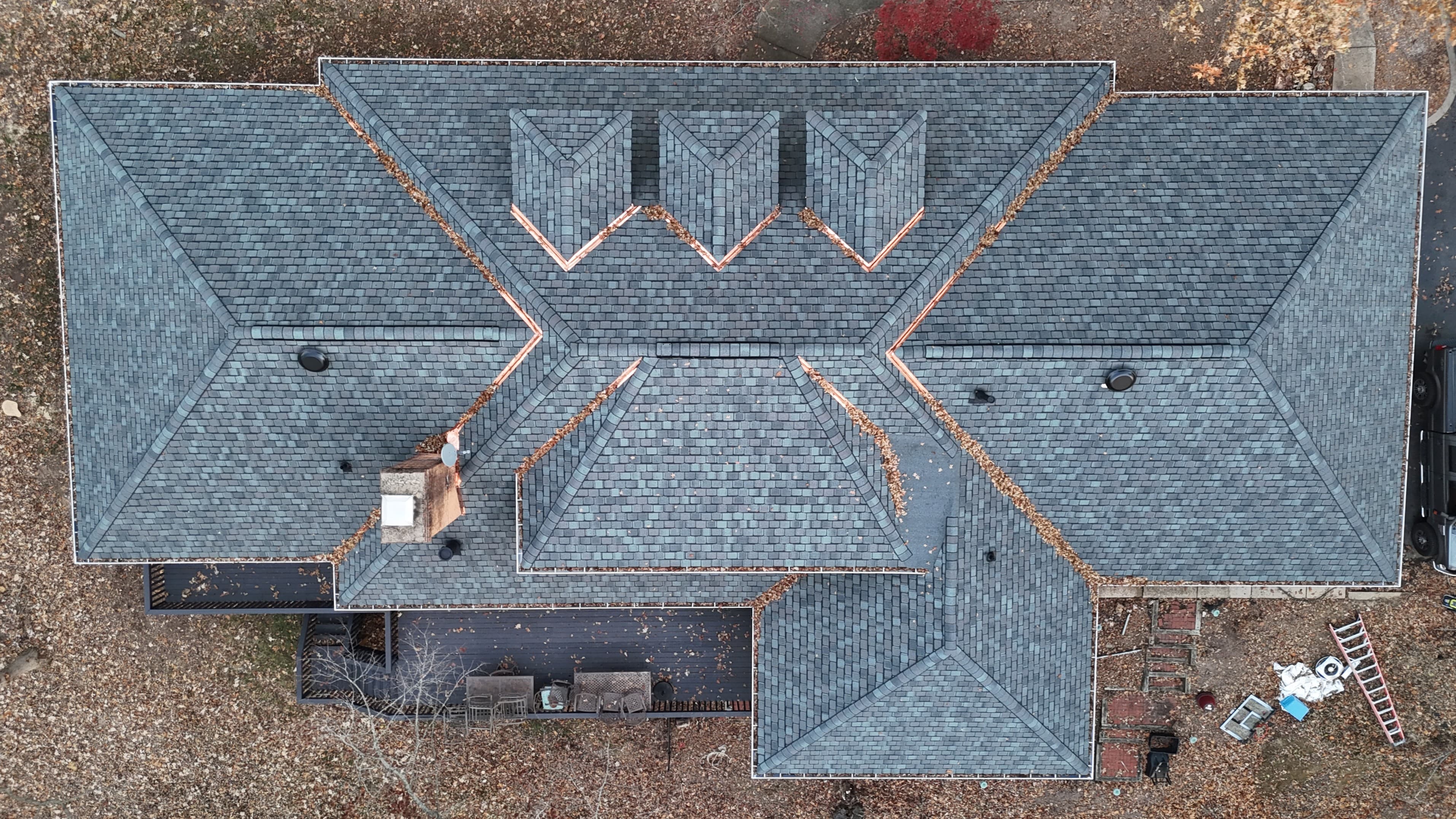 Big Timber project — top-down aerial after restoration showing uniform new dark shingle planes with copper ridge and valley details on three dormers