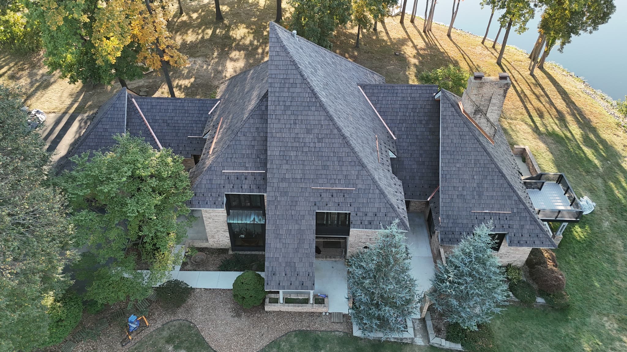 The Architect's Retreat — aerial front elevation after restoration: new dark cedar shake roof with copper ridge and valley details on a multi-gable brick residence in autumn