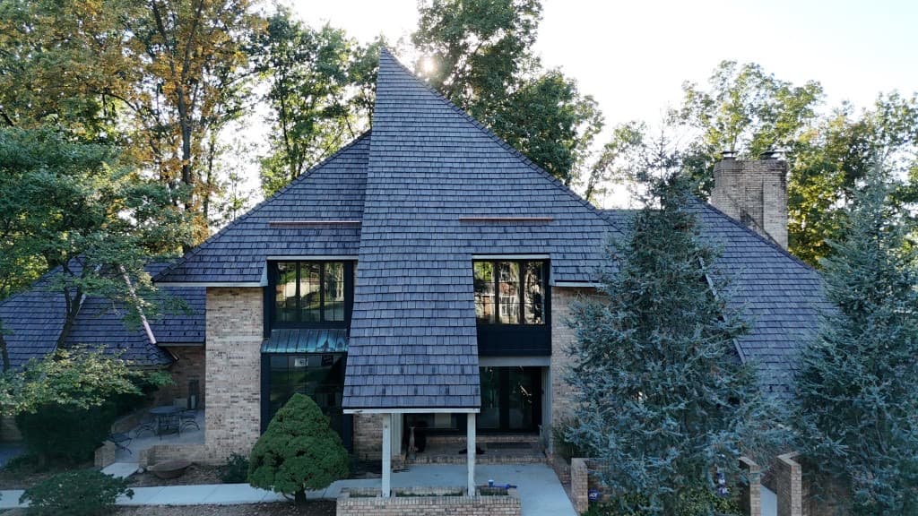 Wide aerial view of a brick residence with multi-gable cedar wood shake roofing and copper flashing