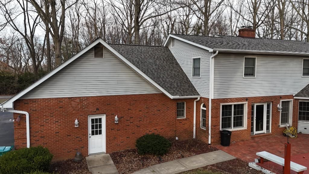 Elevated exterior of a residential home with new architectural shingles, gutters, and mixed brick and siding