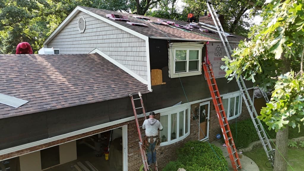 Roofing crew on ladders installing shingles mid-project — active on-site repairs